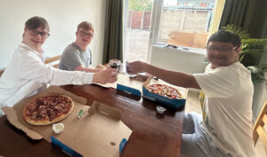 A photo of three young men sat enjoying some takeaway pizza together